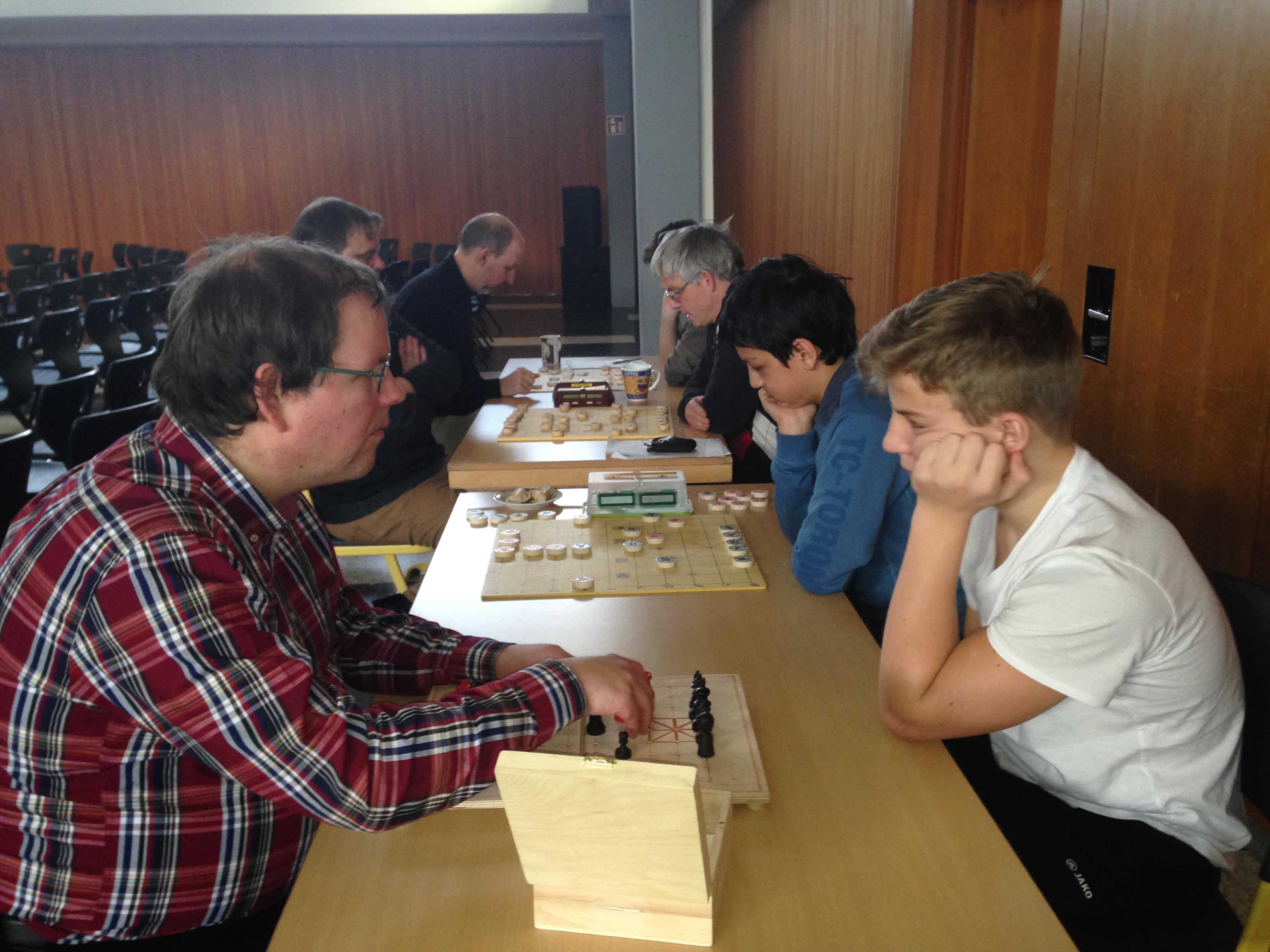 Der blinde Björn (vorne links) hantiert an seinem Spezialbrett; ihm gegenüber sitzt Nick, der als Assistent fungiert. Der Gegner von Björn ist Kai, der am großen Brett neben Nick sitzt.